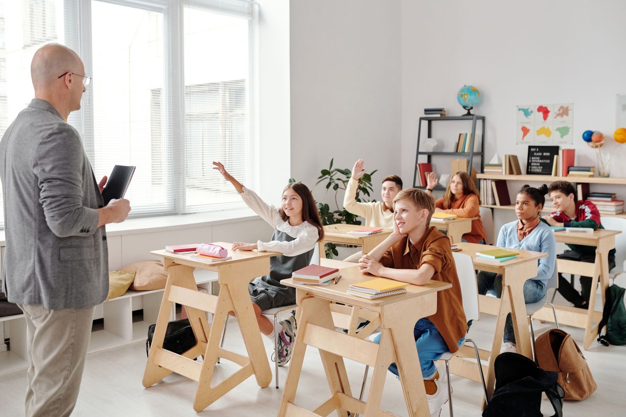 Hello world! Students engage eagerly in a classroom, raising hands and participating in a lesson with their teacher.