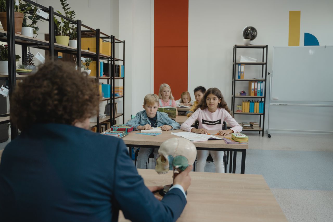 5 ridiculously simple ways to improve your ideas Children learn biology in a colorful classroom setting with a teacher explaining a skull model.