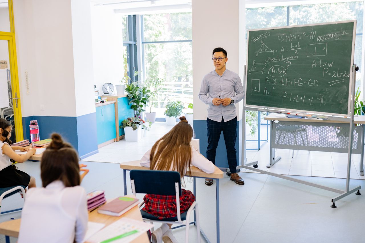 Mastering the First Impression: Your intriguing post title goes here Teacher instructing students in a bright classroom with a blackboard filled with math equations.
