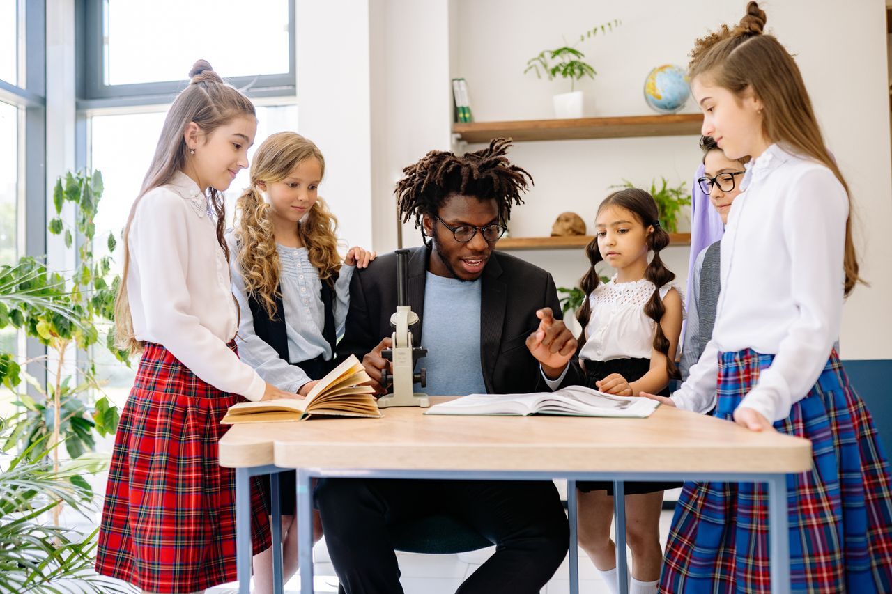Powerfully WordPress theme Teacher and diverse group of students in school setting, learning with books and microscope.